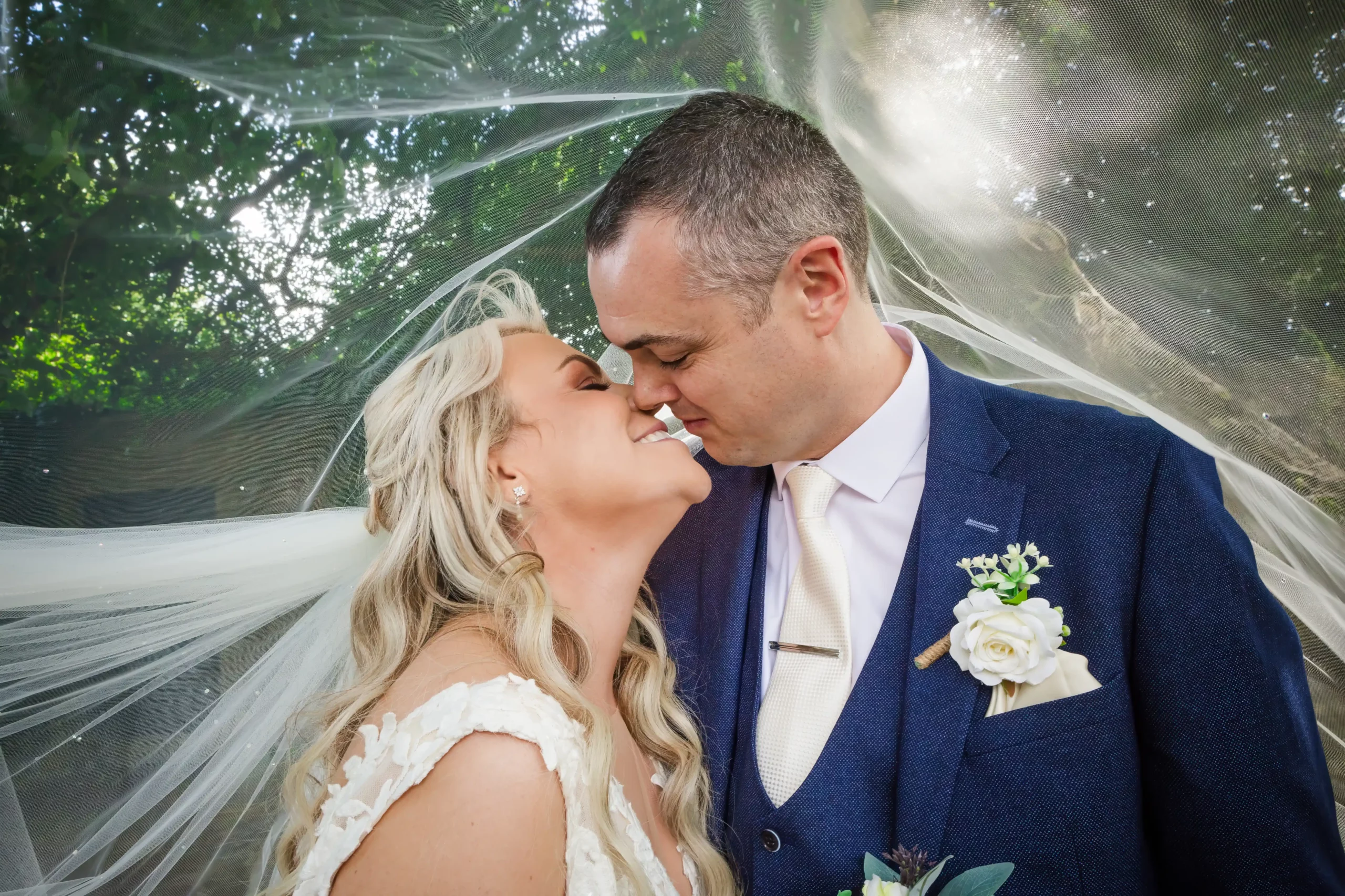 bride and groom kiss as brides veil blows over their heads