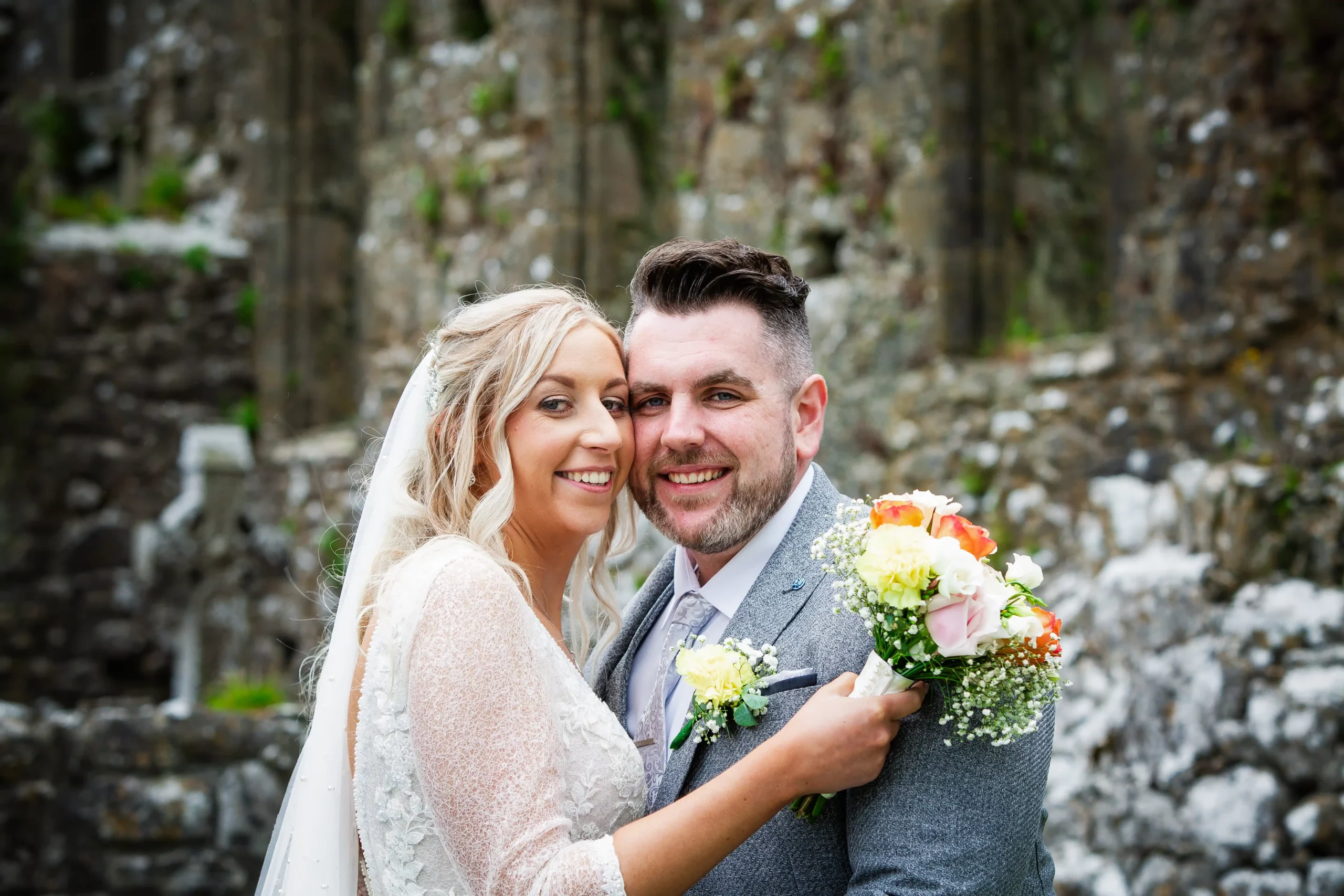 bride and groom with cheeks touching face the camera and smile