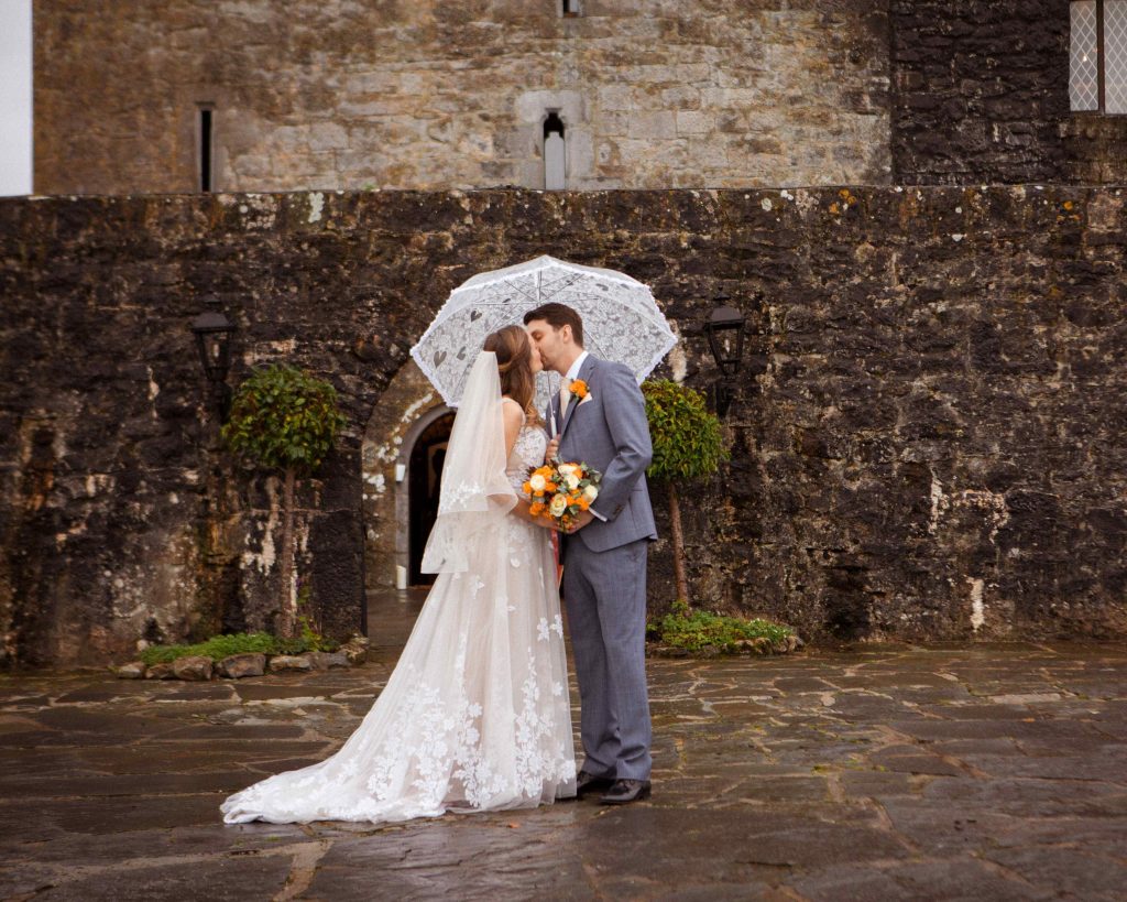 bride and groom stand kissing under a white umbrella