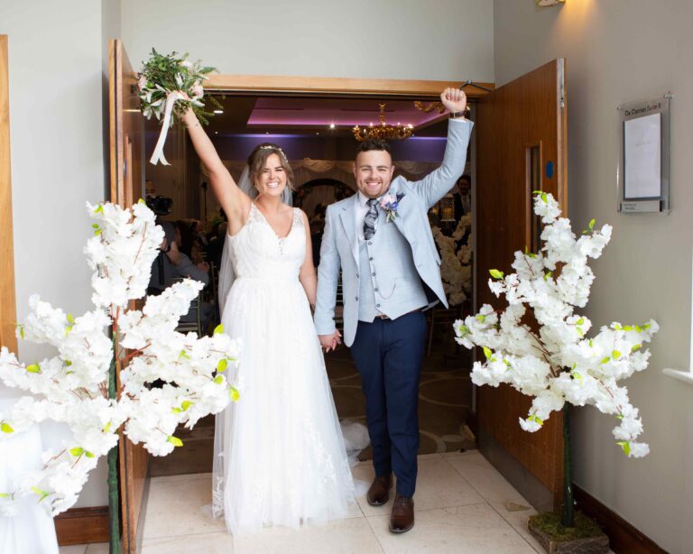 bride and groom walking out a doorway punching the air in happiness