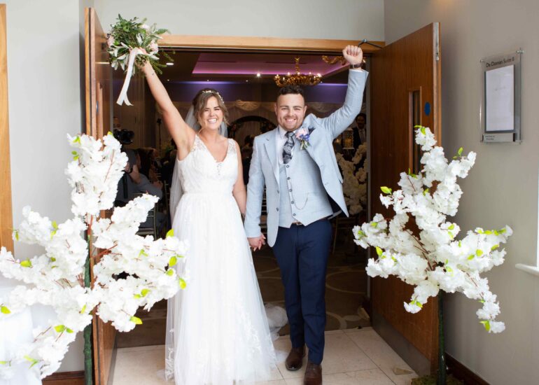 bride and groom walking out a doorway punching the air in happiness