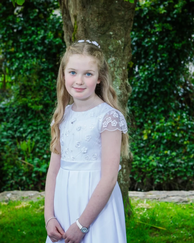 girl on holy communion day stands in front of a tree