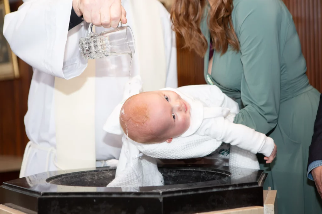 mother holds bsby over font on christening day