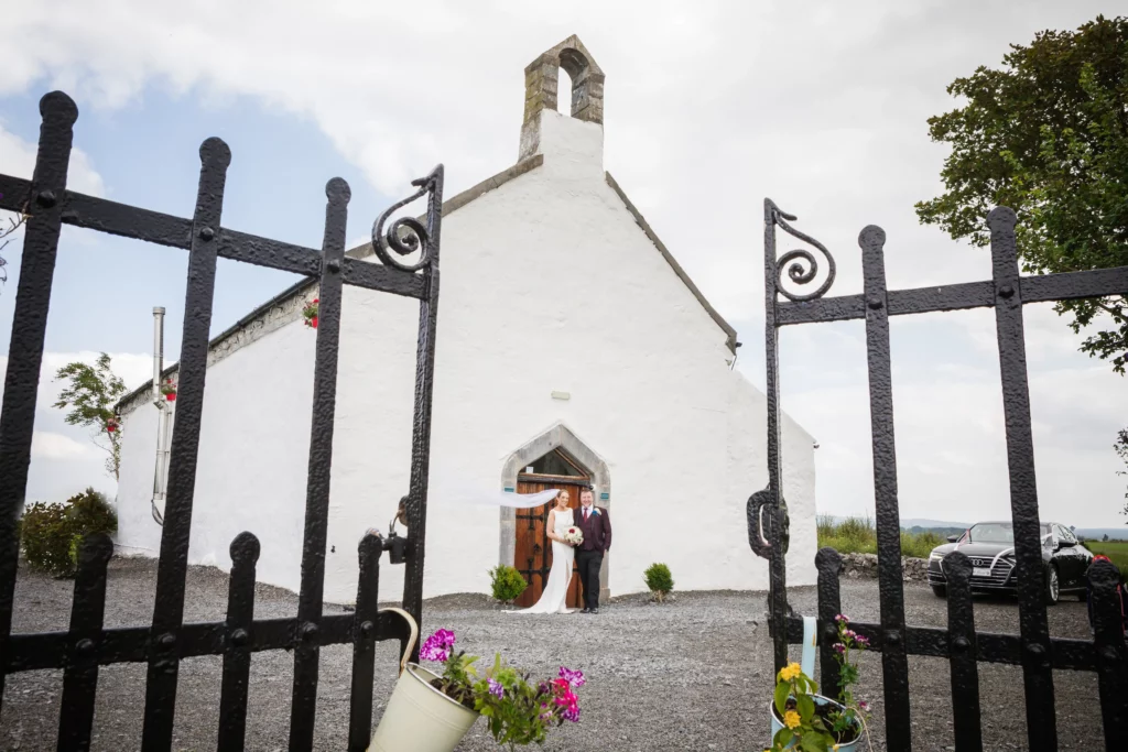 bride and groom standing outside an old whitewashed church with black cast iorn gates in the foreground