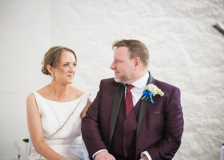 bride and groom sitting in ceremony look at each other and smile