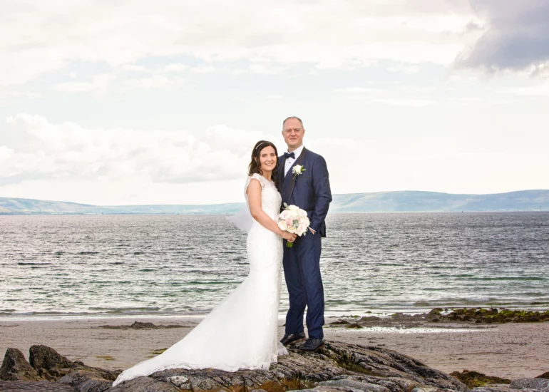 bride and groom standing on a rock at the beach