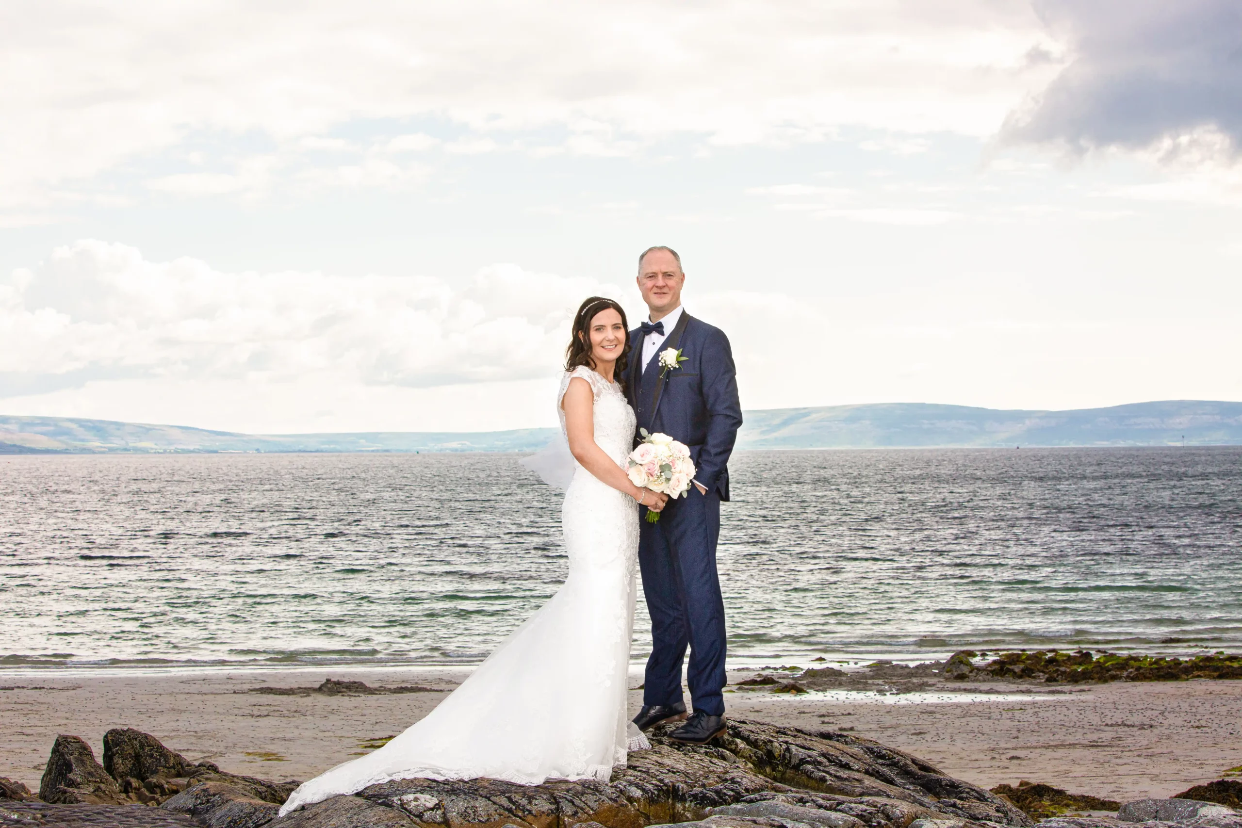 bride and groom standing on a rock at the beach