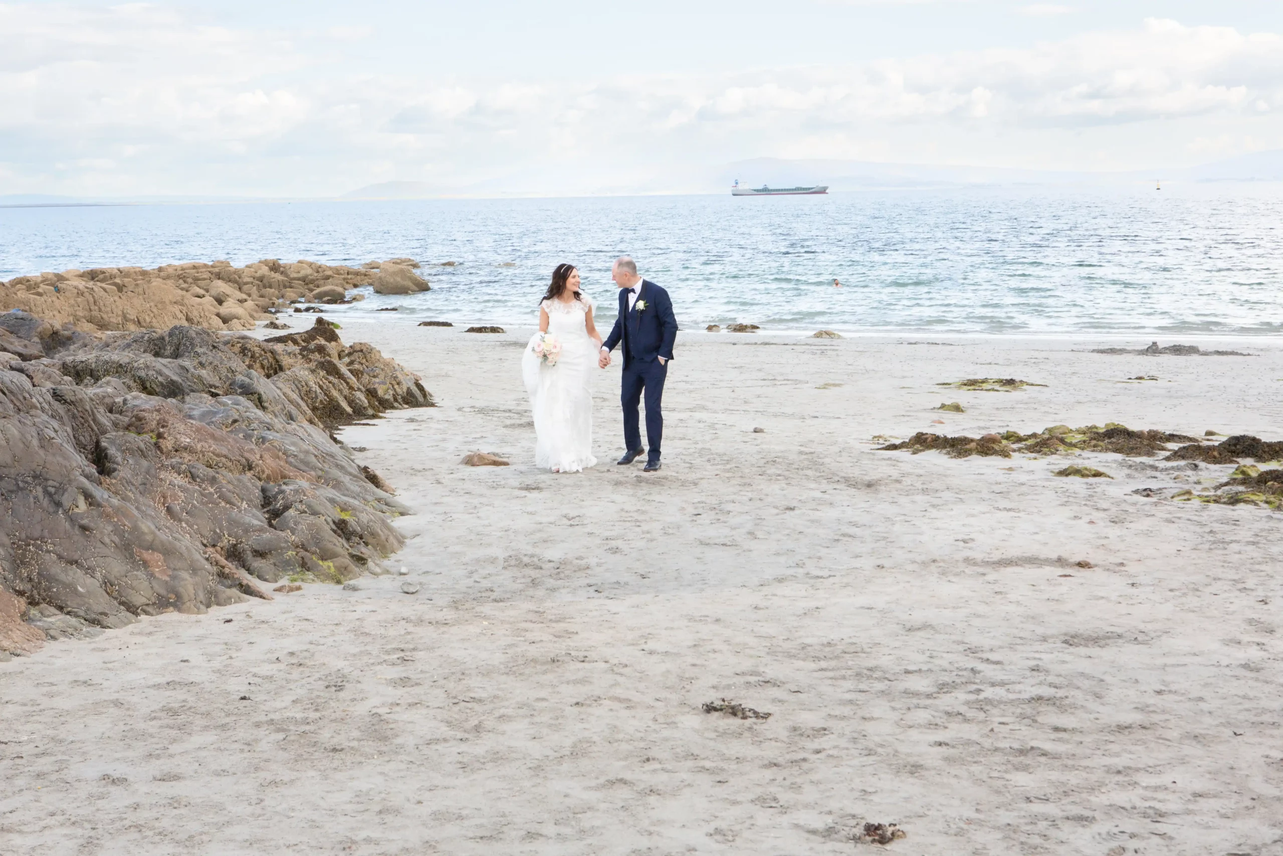 bride and groom walk holding hands on a sandy beach