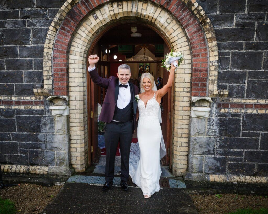 Sharon and Barry raise their arms in celebration outside the Garrison Church in Renmore after their wedding ceremony.