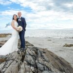 Bride and groom standing on rocks beside Galway Bay in Salthill