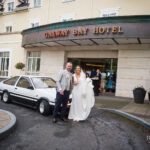 Newlyweds outside Galway Bay Hotel beside a Toyota Twin Cam