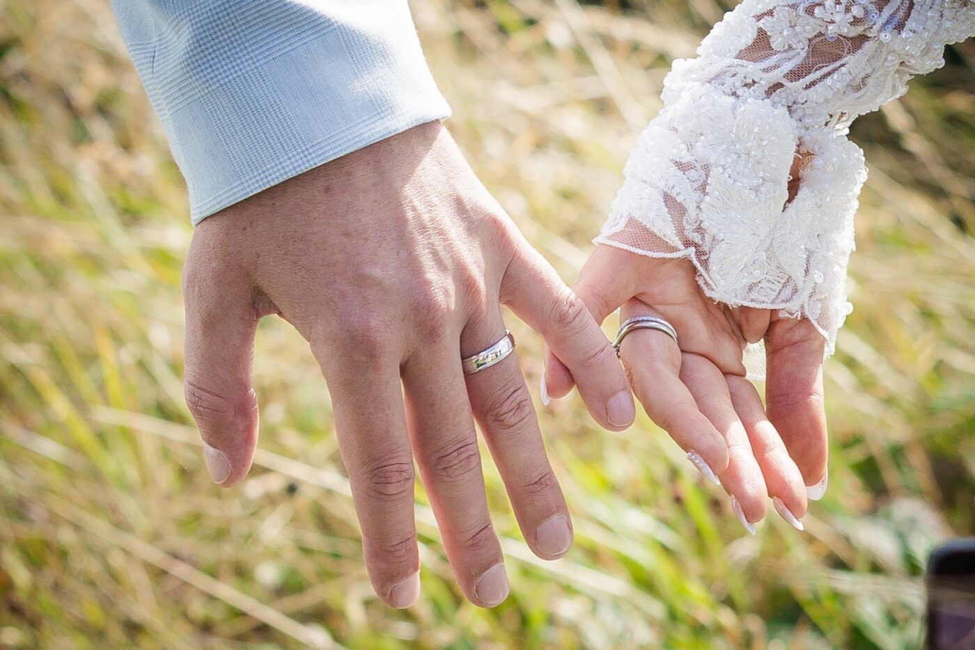 Close-up of the bride and groom linking fingers, showing their wedding rings and the bride’s lace sleeve.