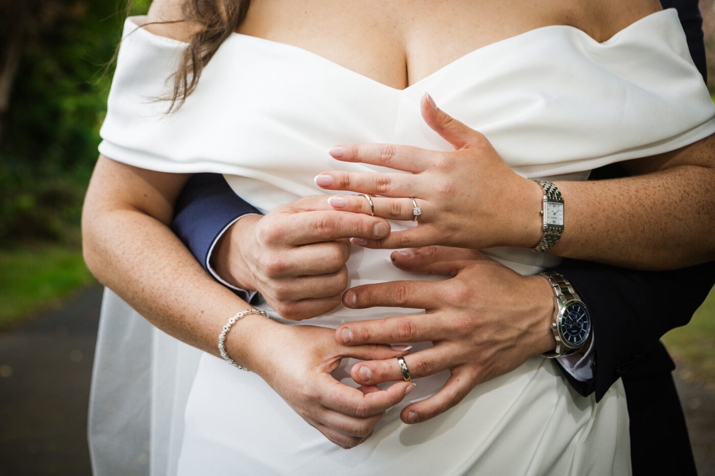 Close-up of the groom embracing the bride, with their hands overlapping to display their wedding and engagement rings.