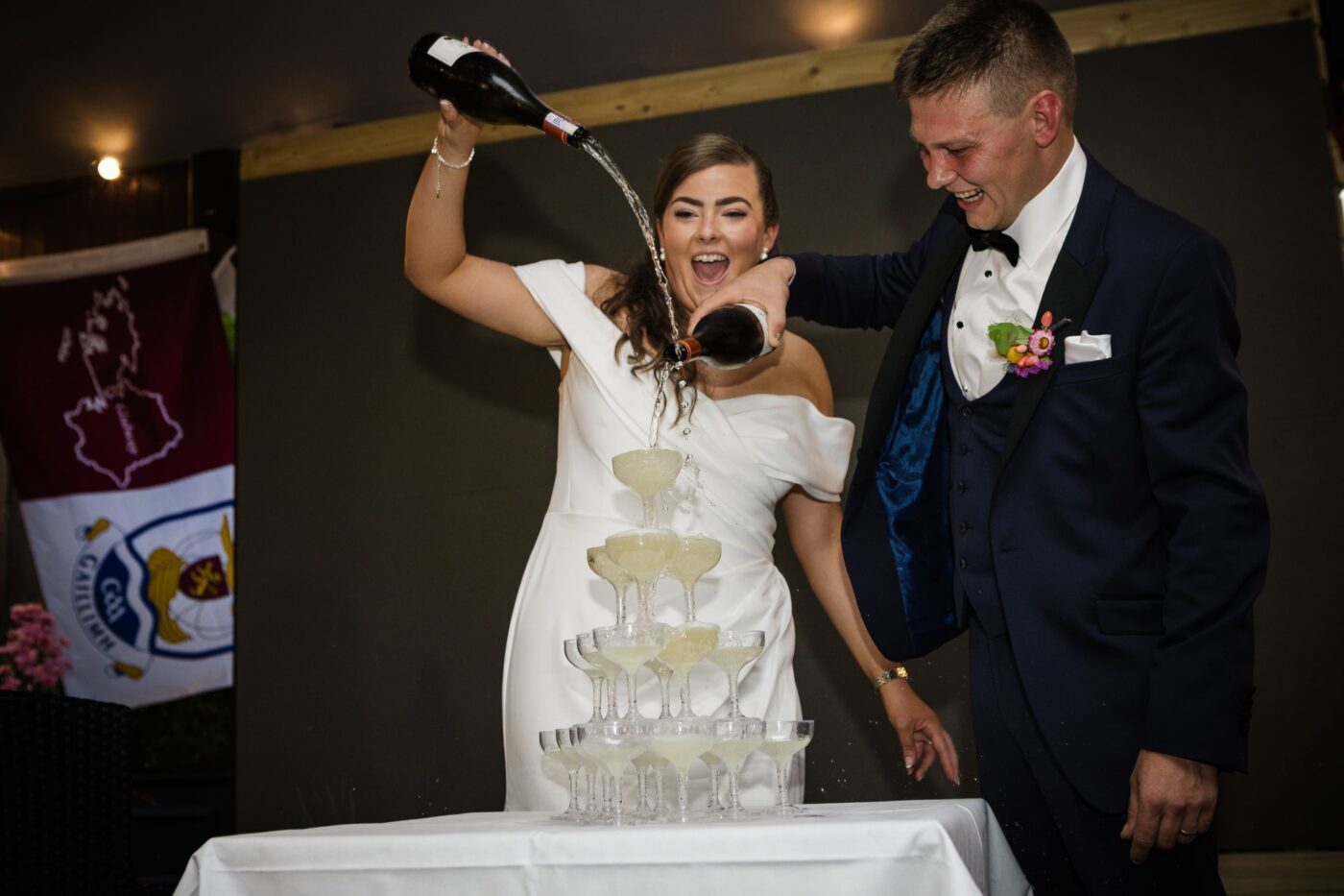 Bride and groom laughing as they pour champagne into a tower of coupe glasses.