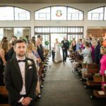 Rory waiting as Áine enters Tynagh Church with her dad and a young boy, surrounded by wedding guests.