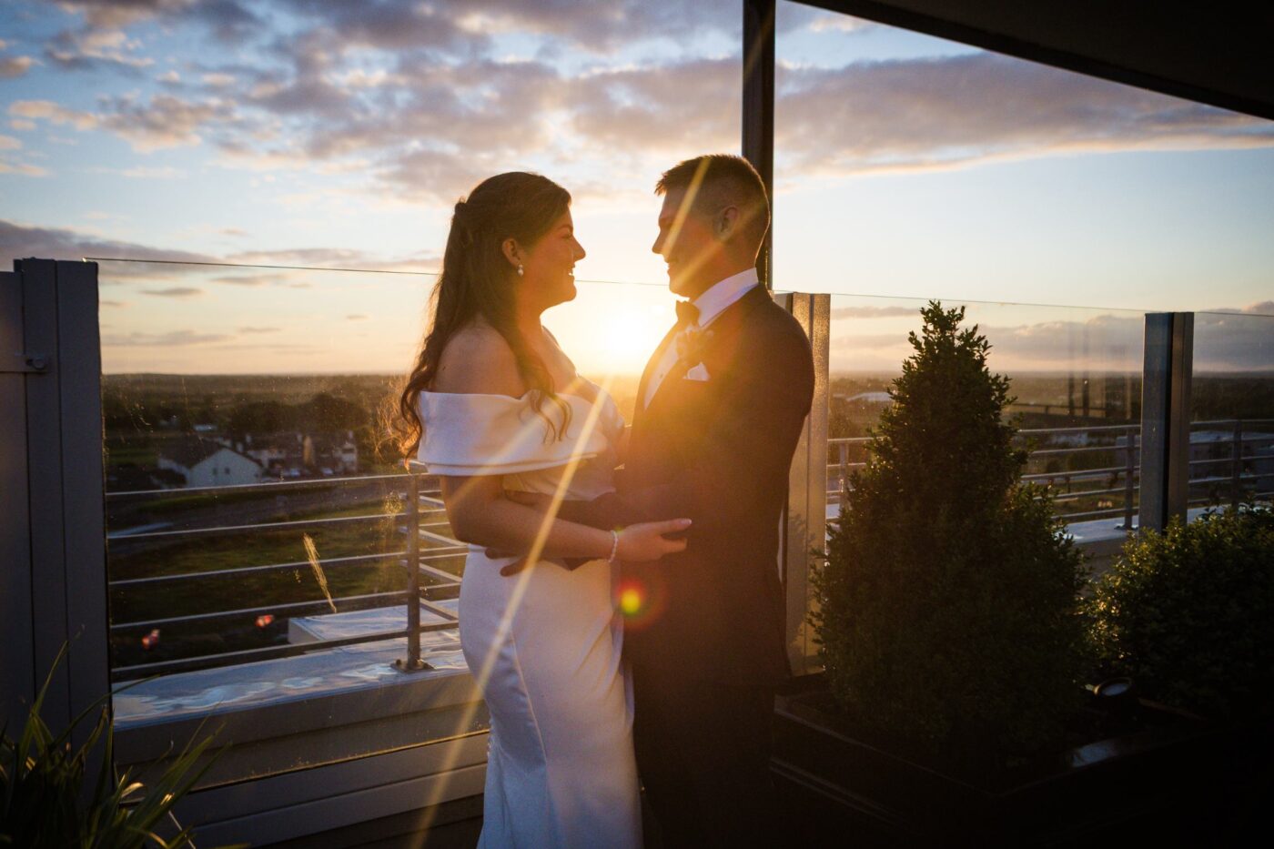 Bride and groom embracing on a rooftop terrace, backlit by the setting sun.