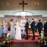 Áine and Rory holding hands at the altar as Father Bohan leads their ceremony in Tynagh Church.