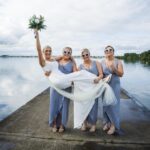 Three bridesmaids wearing heart-shaped sunglasses lift Áine as she raises her bouquet on the pier at Loughrea Lake.