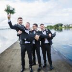 Rory raising a bouquet while his three groomsmen lift him on the pier at Loughrea Lake.