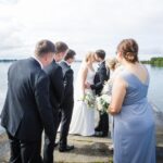 Áine and Rory kissing on the pier at Loughrea Lake, framed by their bridesmaids and groomsmen.
