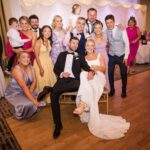 Áine and Rory seated together, surrounded by smiling guests and children at their Loughrea Hotel & Spa reception.