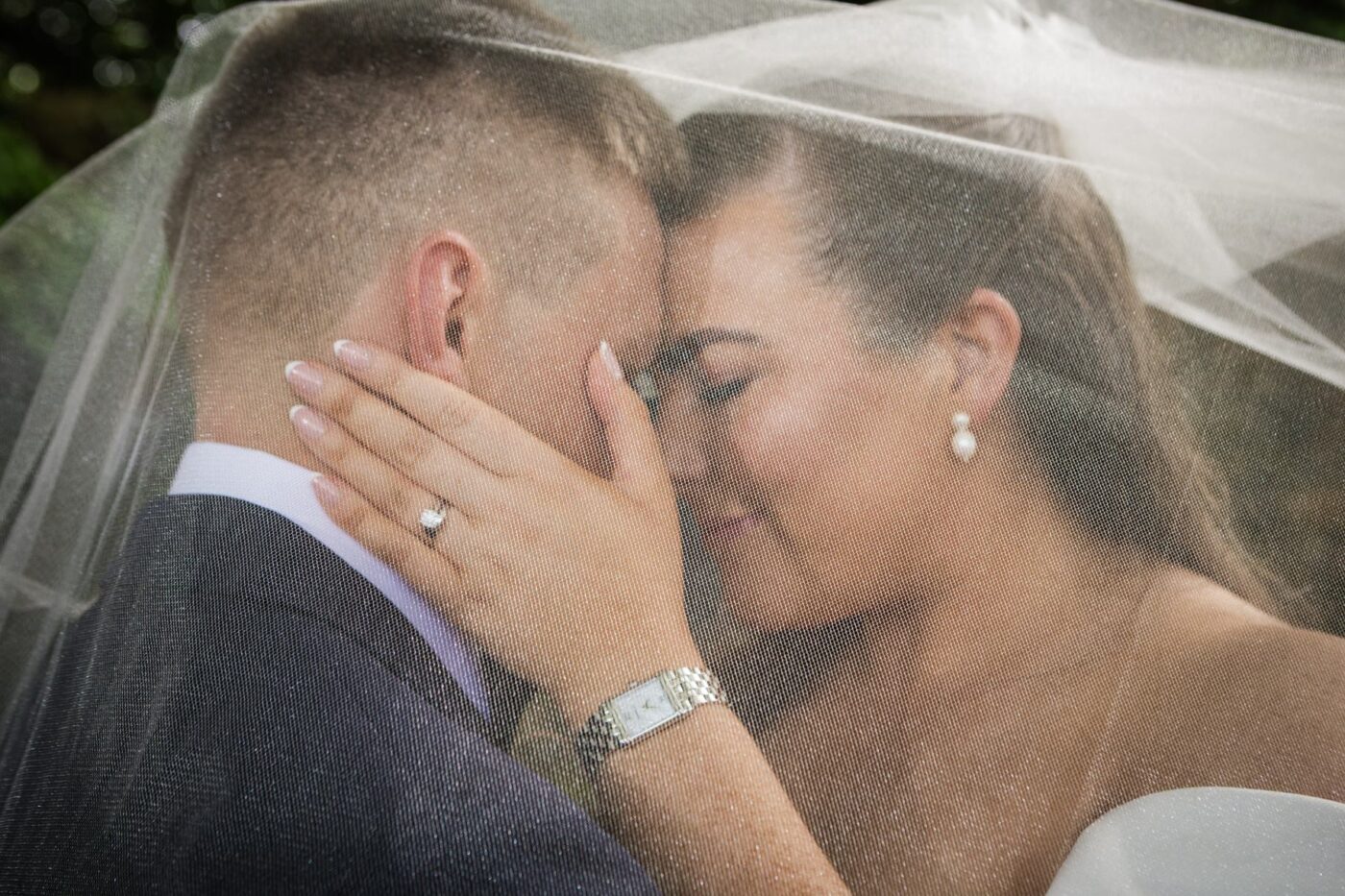 Close-up of bride and groom touching foreheads beneath her veil, with her hand resting against his neck.