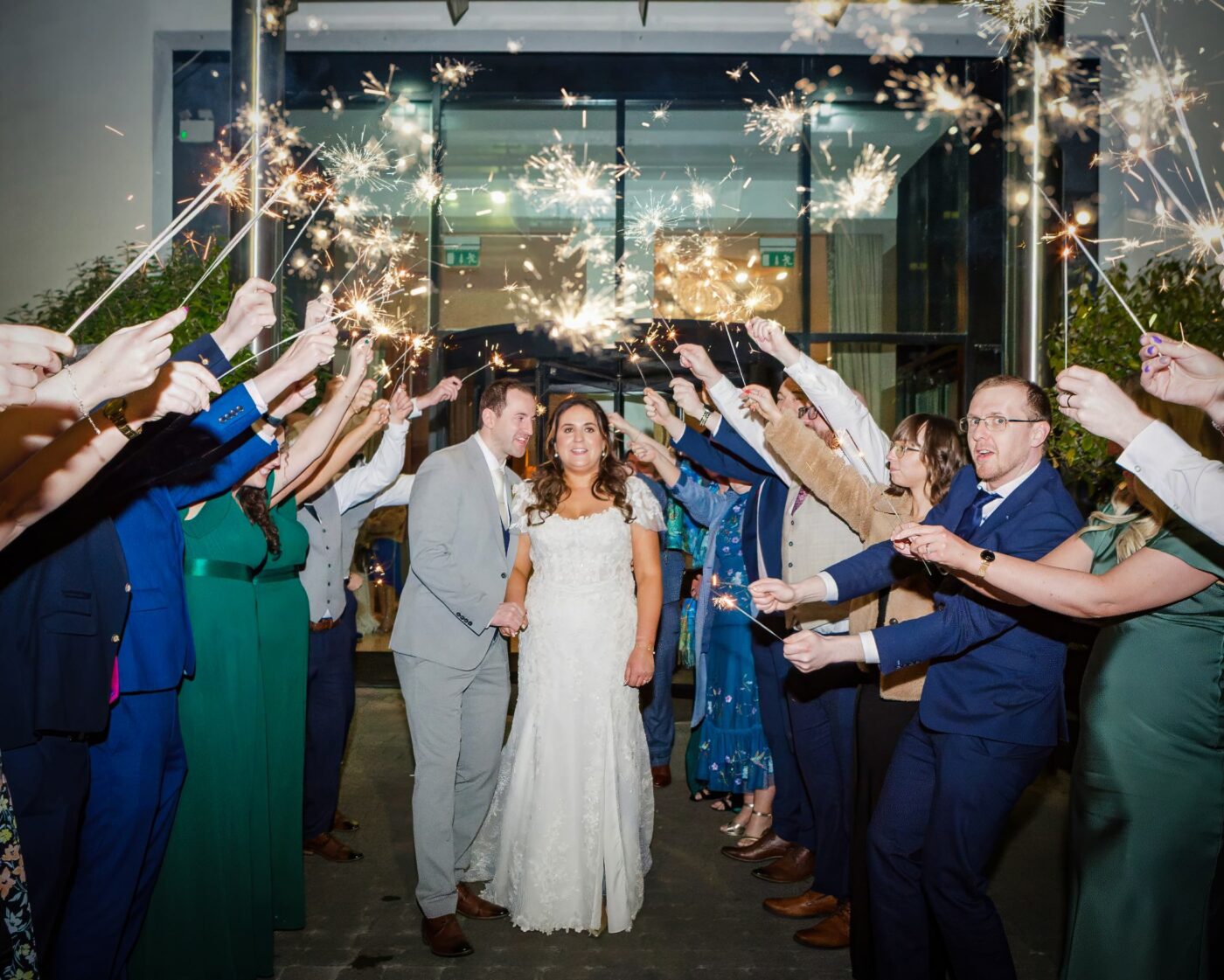Bride and groom holding hands beneath an arch of sparklers held by wedding guests outside the entrance to Loughrea Hotel & Spa.