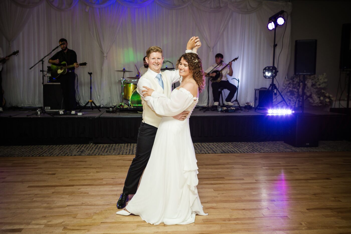 Bride and groom dancing together on a wooden dance floor at Loughrea Hotel & Spa, with a live band performing behind them.