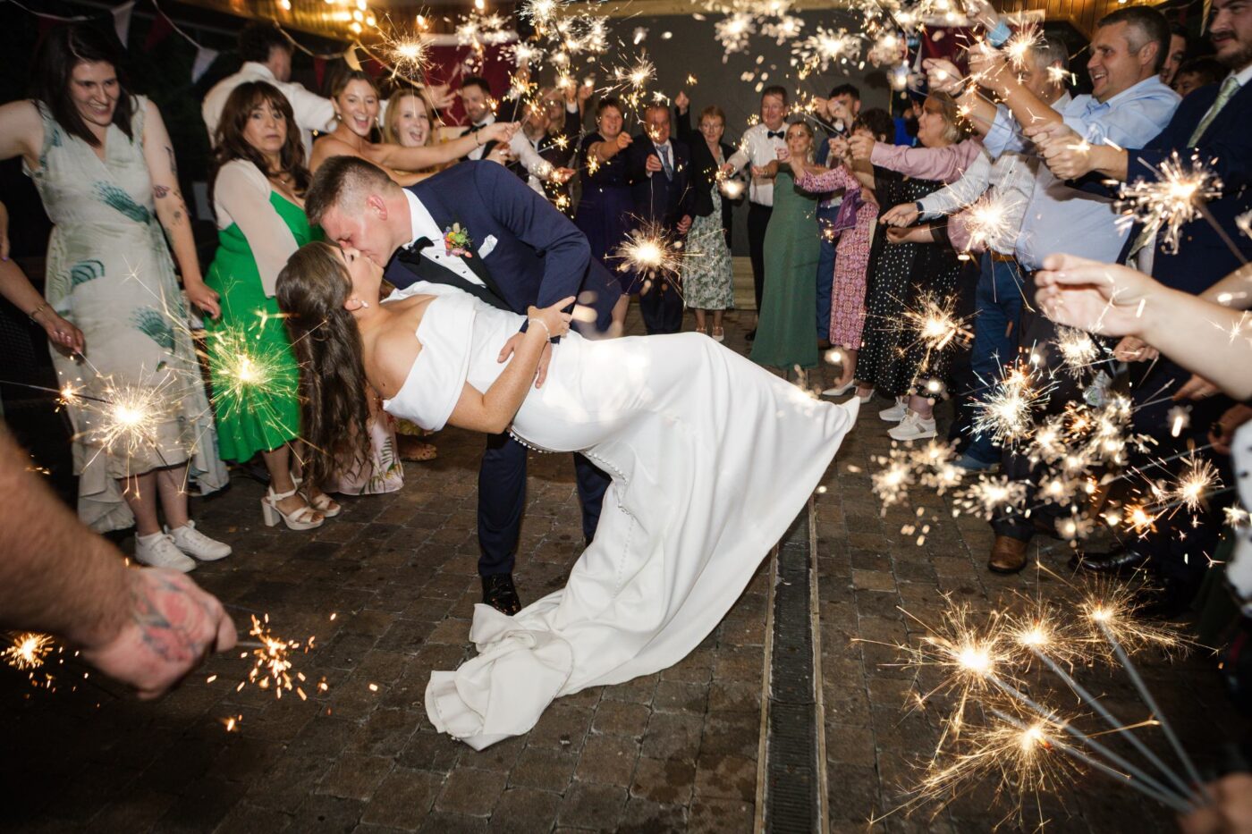 Groom dipping and kissing the bride between two rows of wedding guests holding glowing sparklers at Loughrea Hotel & Spa.