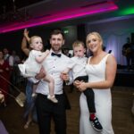 Áine and Rory holding two young children on the dance floor at Loughrea Hotel & Spa, with guests and the live band behind them