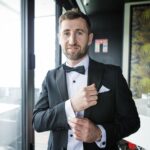 Rory adjusting his cufflink beside a window at Loughrea Hotel & Spa, wearing a black tuxedo and bow tie.