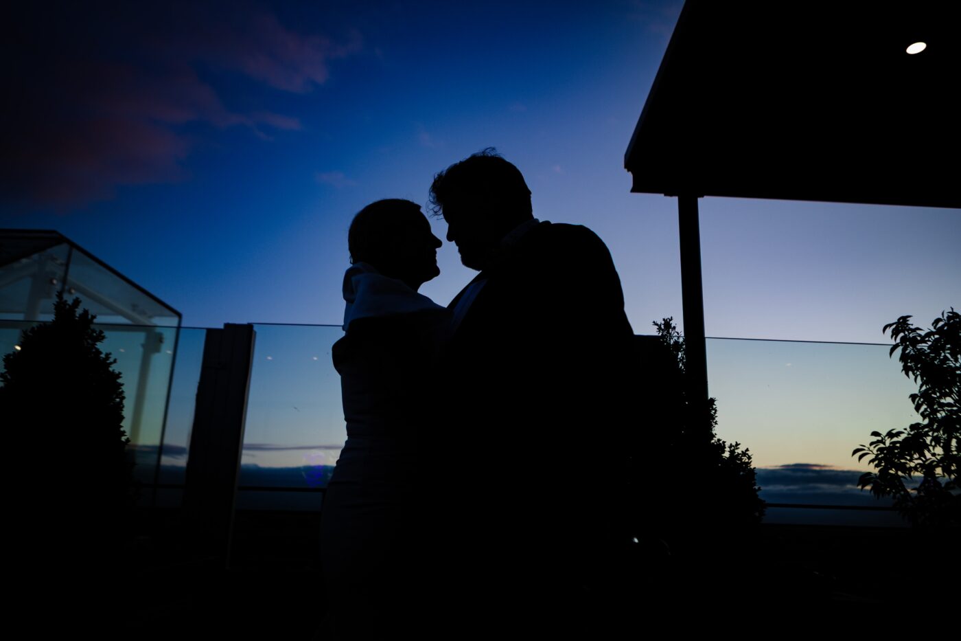 Silhouette of bride and groom embracing on the rooftop terrace at Loughrea Hotel & Spa beneath a deep blue evening sky.
