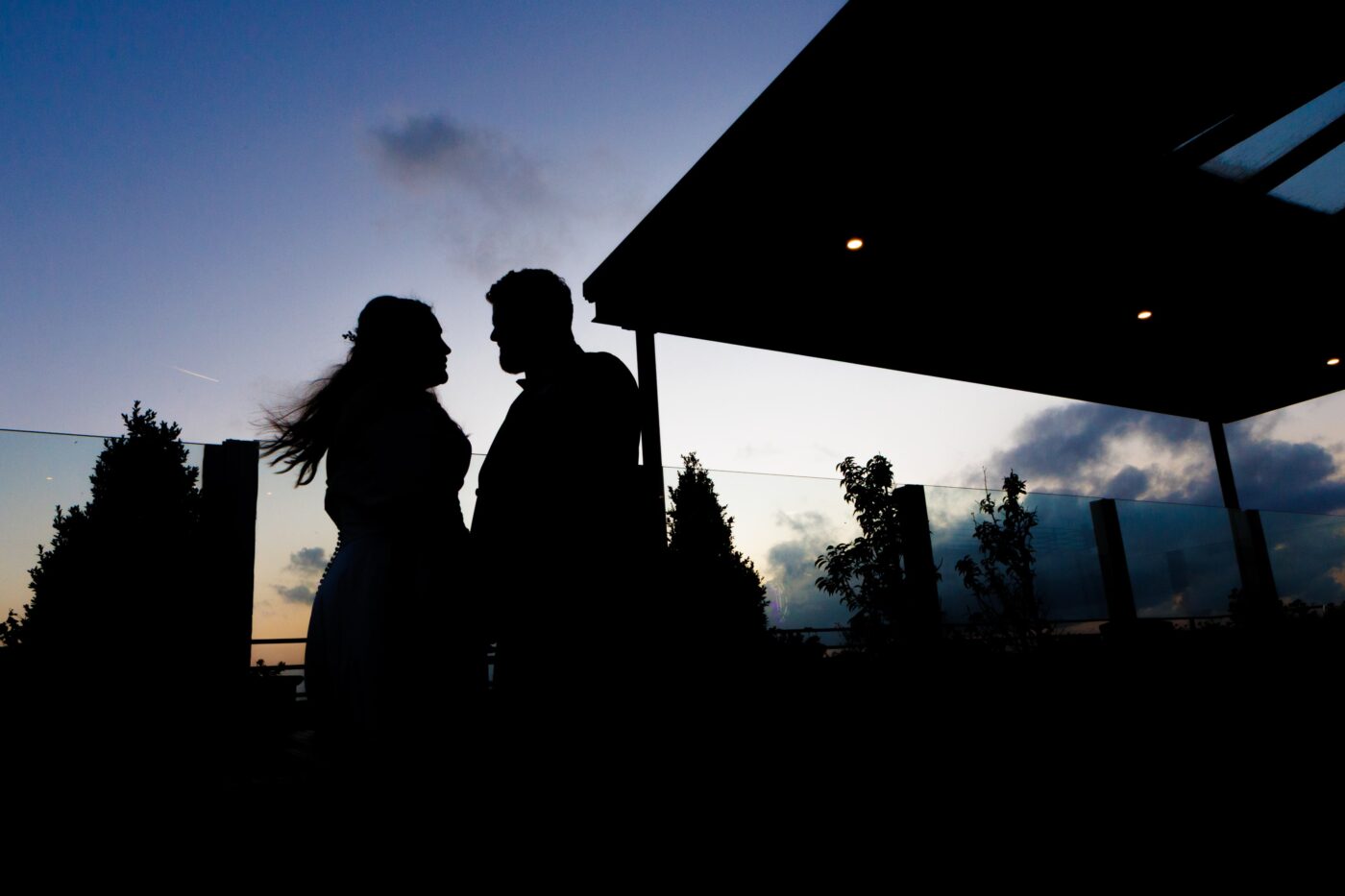 Bride and groom facing each other in silhouette on the rooftop terrace at Loughrea Hotel & Spa beneath a cloudy evening sky.