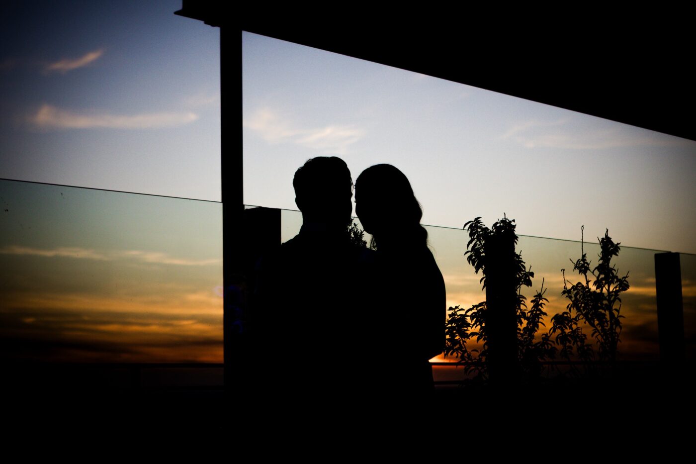 Bride and groom standing close together in silhouette on the rooftop terrace at Loughrea Hotel & Spa against an orange sunset.