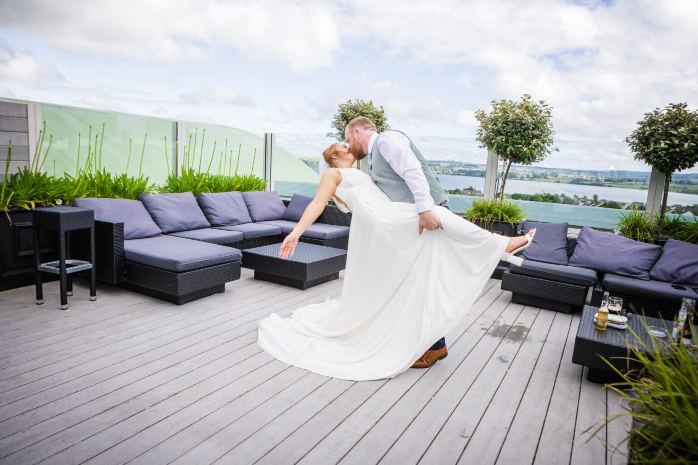 Groom dipping and kissing the bride on the rooftop terrace at Loughrea Hotel & Spa, with outdoor seating and lake views.