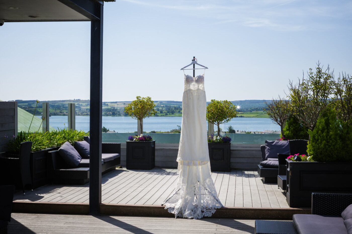 Lace wedding dress hanging between potted trees on the rooftop terrace at Loughrea Hotel & Spa, with Loughrea Lake and countryside behind it.