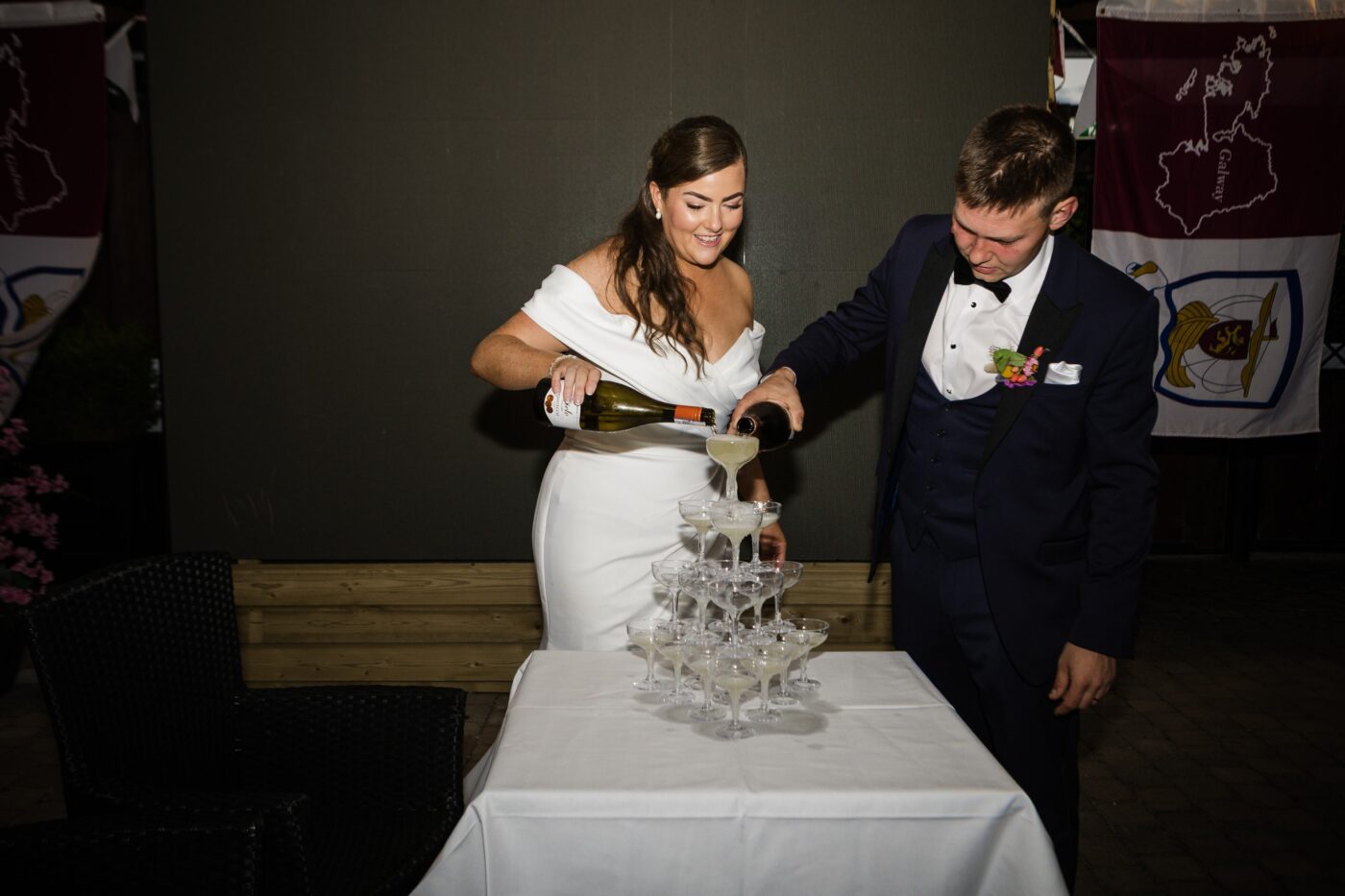 Bride and groom pouring sparkling wine together into the top glass of a champagne tower at Loughrea Hotel & Spa.
