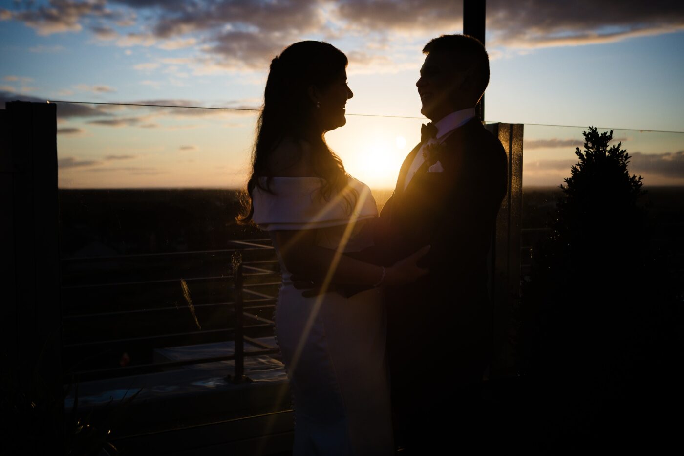 Bride and groom smiling at each other on the rooftop terrace at Loughrea Hotel & Spa, backlit by the setting sun.