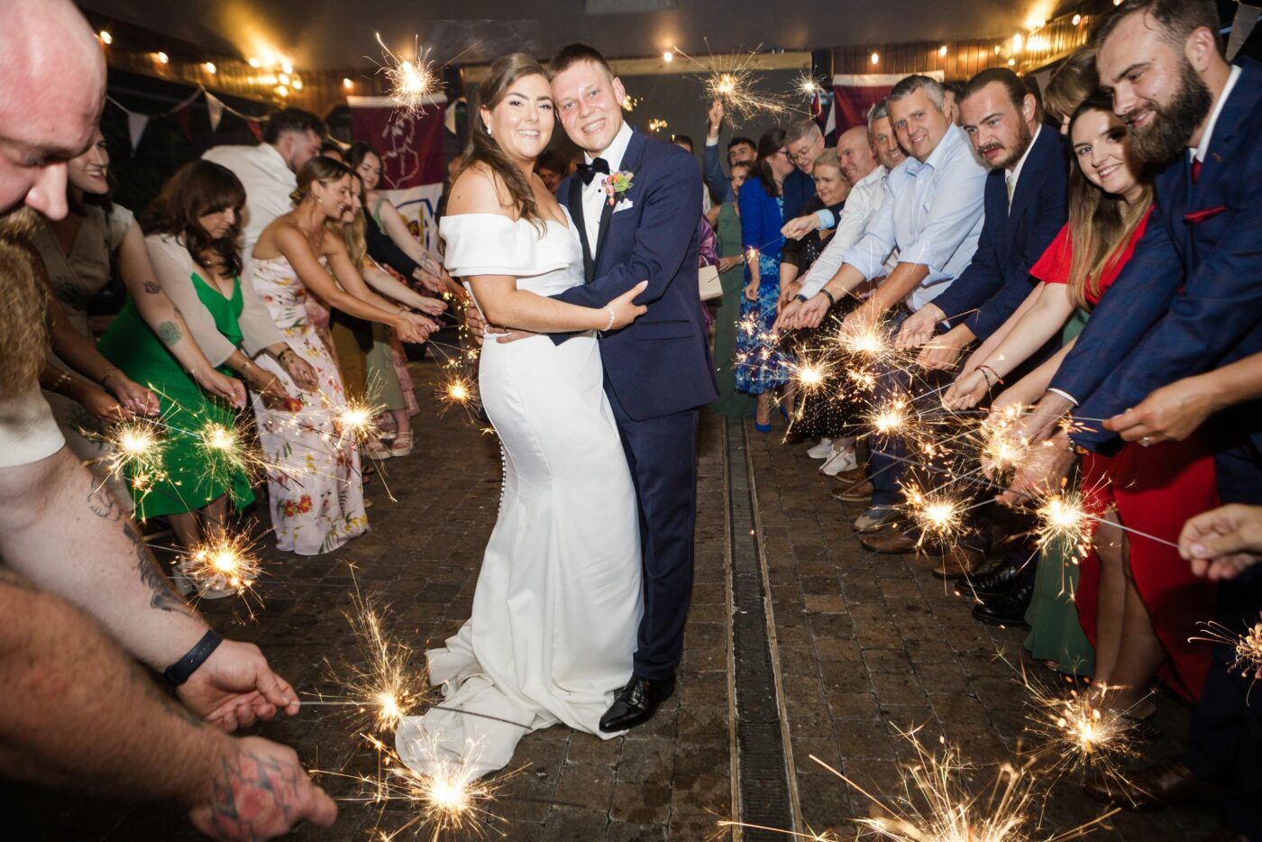 Bride and groom embracing between two rows of smiling wedding guests holding glowing sparklers at Loughrea Hotel & Spa.